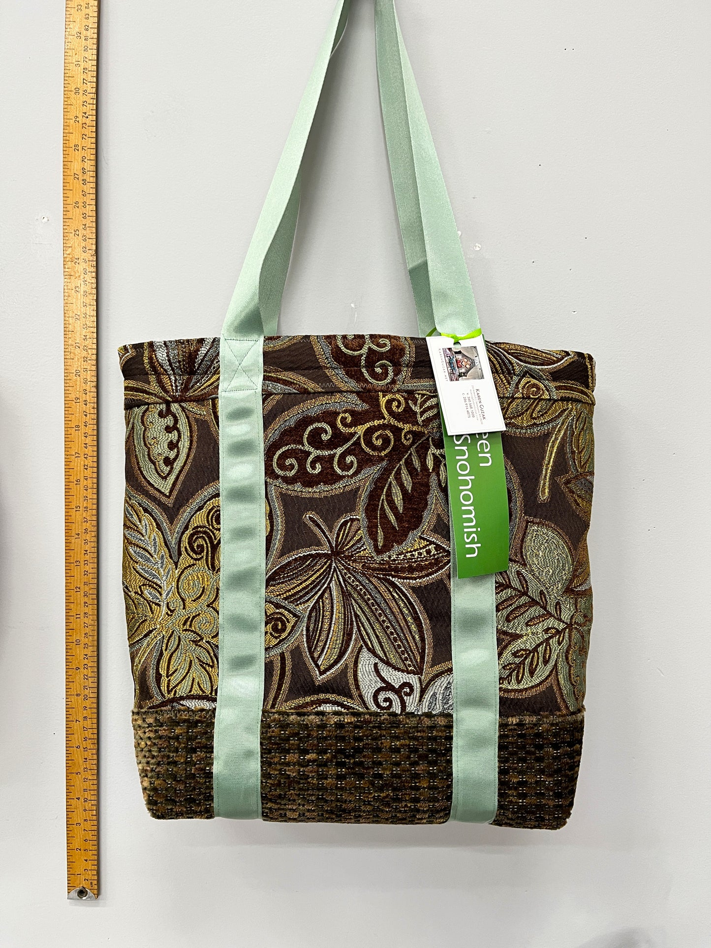 Patterned tote bag with green straps and a visible brand tag, next to a ruler for scale.