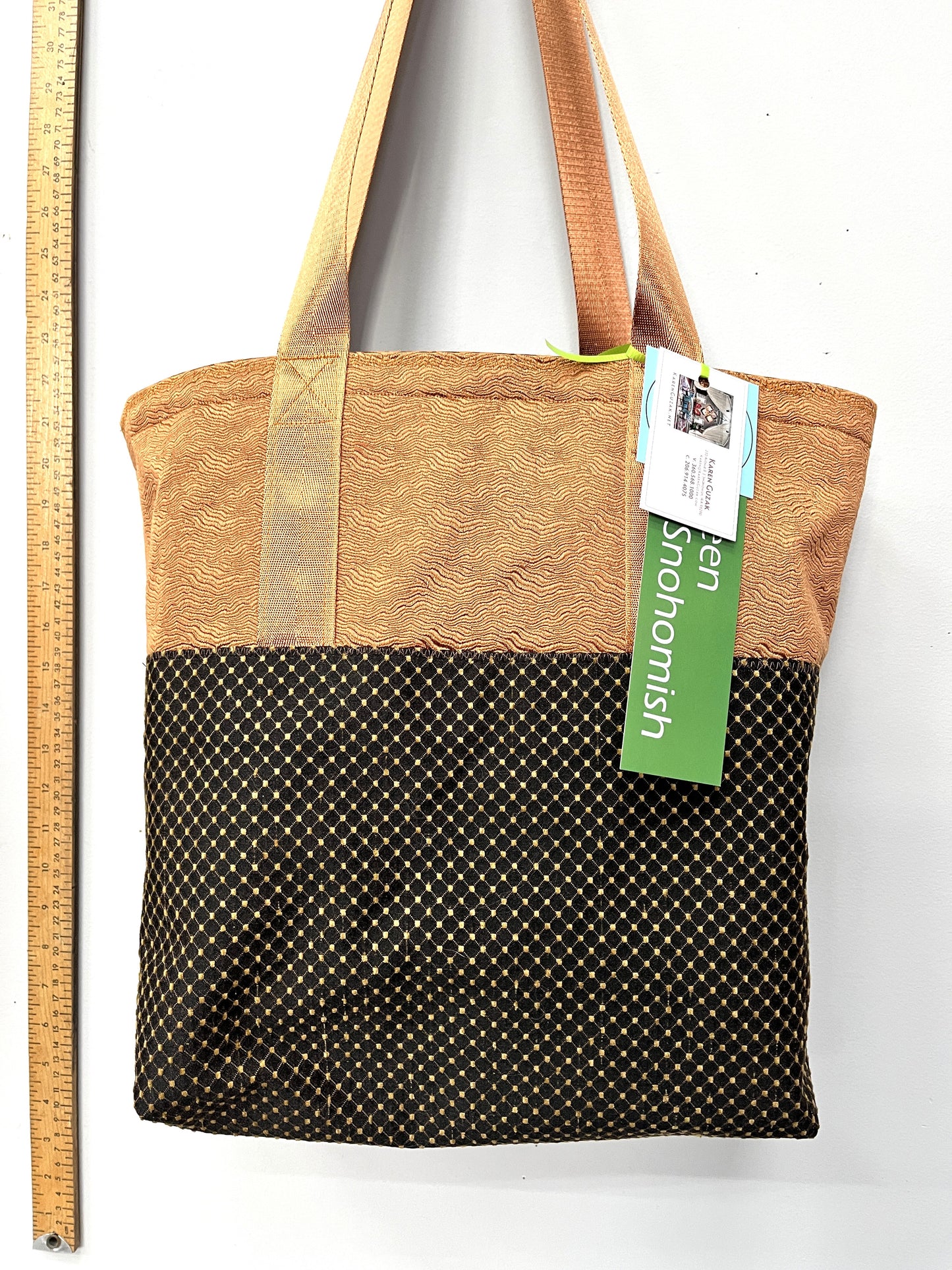 Tote bag with brown top section and black bottom section with gold polka dots, on a white background with a ruler for scale.
